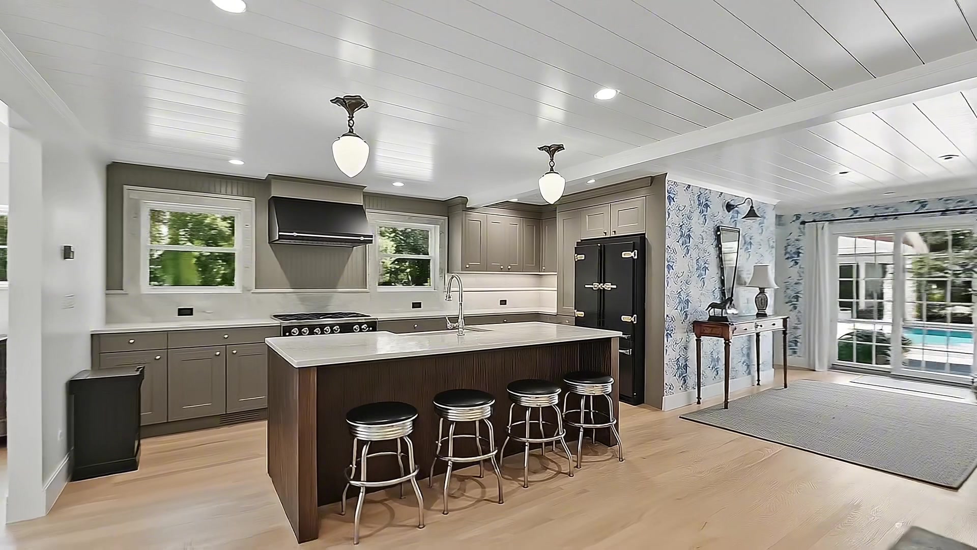 Chef's kitchen with large center island, dark wood base and marble countertop, metal bar stools, gray-green custom cabinetry, pendant lighting, and shiplap ceiling
